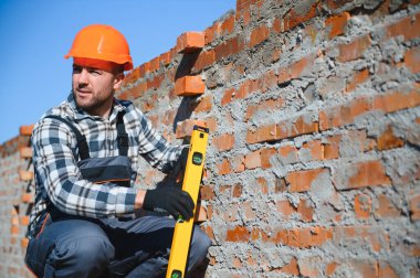 Tuğla duvar kuruluyor. Üniformalı inşaat işçisi ve güvenlik ekipmanı inşaatında çalışıyor.