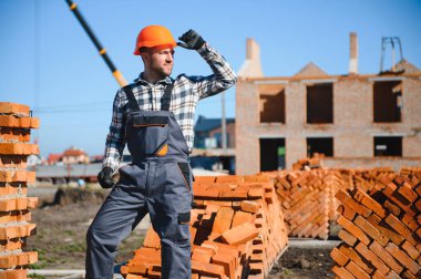 Tuğla duvar kuruluyor. Üniformalı inşaat işçisi ve güvenlik ekipmanı inşaatında çalışıyor.