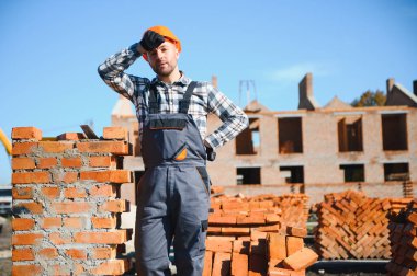 Tuğla duvar kuruluyor. Üniformalı inşaat işçisi ve güvenlik ekipmanı inşaatında çalışıyor.