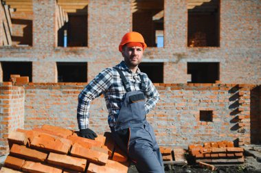 İnşaat alanında tuğla taşıyan genç bir inşaatçı..