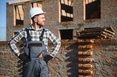 Kırmızı tuğlalı ev inşaatında üniformalı ve kasklı bir erkek inşaat işçisi..