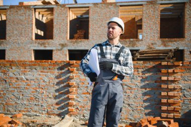 Tuğladan evler inşa eden bir mimar ya da mühendis inşaat planını elinde tutuyor ve işlerin nasıl yürüdüğünü kontrol ediyor..