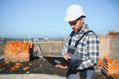 Tuğla duvar kuruluyor. Üniformalı inşaat işçisi ve güvenlik ekipmanı inşaatında çalışıyor.