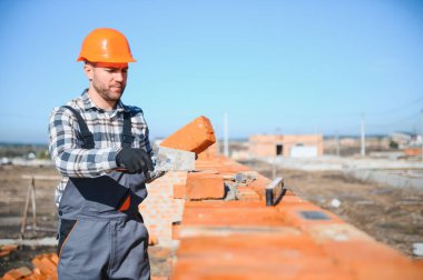 Tuğla duvar kuruluyor. Üniformalı inşaat işçisi ve güvenlik ekipmanı inşaatında çalışıyor.