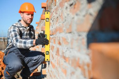 Kırmızı tuğlalı ev inşaatında üniformalı ve kasklı bir erkek inşaat işçisi..