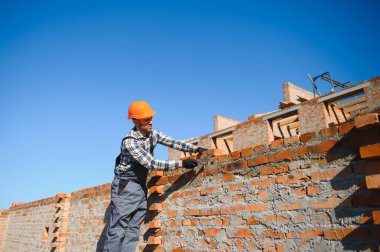 Tuğla duvar kuruluyor. Üniformalı inşaat işçisi ve güvenlik ekipmanı inşaatında çalışıyor.
