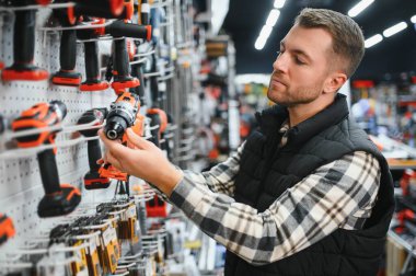Bir adam hırdavatçıdan elektrikli bir alet seçer..