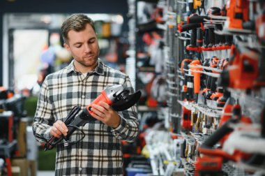 Bir adam hırdavatçıdan elektrikli bir alet seçer..