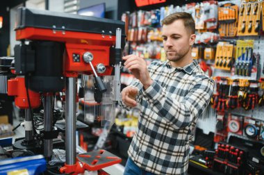 Erkek bir alıcı hırdavatçıdan elektrikli aletler seçer. Büyük bir araç seçimi.