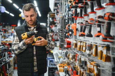 Elektirikli tornavida tutan ve seçen adam, inşaat dükkanında duruyor..