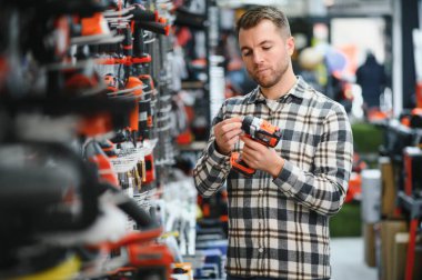 Genç sakallı adamın portresi, aletin içinde dururken modern elektrikli matkap alıyor. Donanım inşaat alanı nesneleri kavramı.