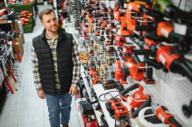 Genç sakallı adamın portresi, aletin içinde dururken modern elektrikli matkap alıyor. Donanım inşaat alanı nesneleri kavramı.