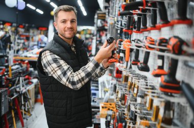 Elektirikli tornavida tutan ve seçen adam, inşaat dükkanında duruyor..