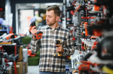 Elektirikli tornavida tutan ve seçen adam, inşaat dükkanında duruyor..