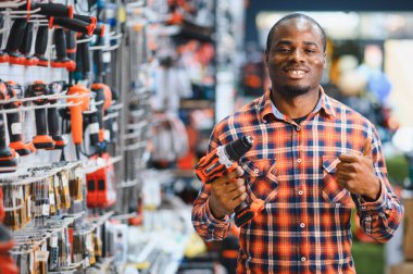 Afrikalı Amerikalı adam aletin içinde dururken modern elektrikli matkap satın alıyor. Donanım inşaat alanı nesneleri kavramı.