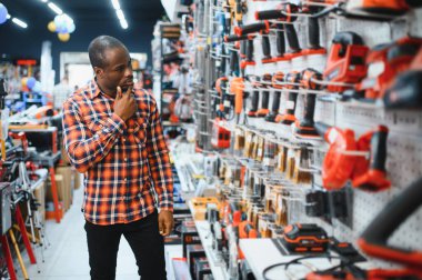 Afrikalı Amerikalı adam aletin içinde dururken modern elektrikli matkap satın alıyor. Donanım inşaat alanı nesneleri kavramı.