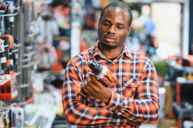 Afrikalı Amerikalı adam aletin içinde dururken modern elektrikli matkap satın alıyor. Donanım inşaat alanı nesneleri kavramı.