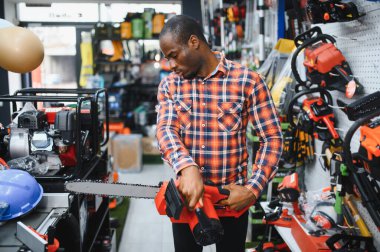 Afrika kökenli Amerikalı adam alet deposunda elektrikli testere tutuyor..