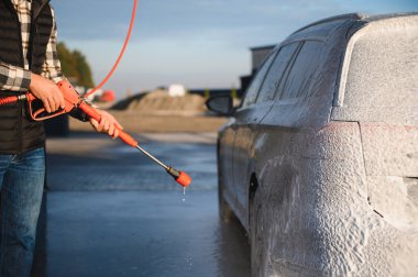 Bir adam arabayı yıkarken köpüğü yıkar. Bir araç araba yıkama sırasında sabunlu köpüğe bulanır, lastikleri, tekerlekleri, kaputu ve arabanın tüm dış kısmını kaplar. self-servis araba yıkama
