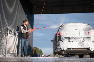 Bir adam arabayı yıkarken köpüğü yıkar. Bir araç araba yıkama sırasında sabunlu köpüğe bulanır, lastikleri, tekerlekleri, kaputu ve arabanın tüm dış kısmını kaplar. self-servis araba yıkama