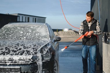 Araba yıkama ekipmanı. Bir adam oto yıkamada araba yıkarken yüksek basınçlı araç yıkama makinesi köpük püskürtür..