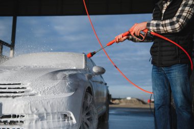 Bir adam arabayı yıkarken köpüğü yıkar. Bir araç araba yıkama sırasında sabunlu köpüğe bulanır, lastikleri, tekerlekleri, kaputu ve arabanın tüm dış kısmını kaplar. self-servis araba yıkama