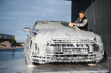 Bir adam oto yıkamada bir arabayı süngerle yıkar..