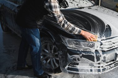 Bir adam oto yıkamada bir arabayı süngerle yıkar..
