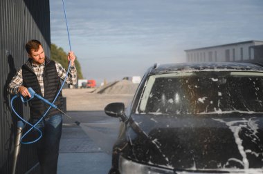 Bir adam arabasını tazyikli suyla yıkama makinesinde yıkıyor..