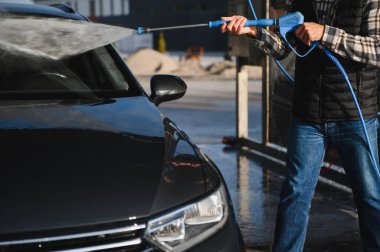 Adam yüksek basınçlı çamaşır makinesinden çıkan suyla araba yıkıyor..