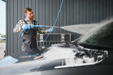 Bir oto yıkama işçisi araba yıkama için yüksek basınçlı su tabancası kullanır..