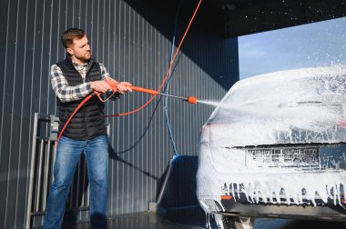 Bir adam arabayı yıkarken köpüğü yıkar. Bir araç araba yıkama sırasında sabunlu köpüğe bulanır, lastikleri, tekerlekleri, kaputu ve arabanın tüm dış kısmını kaplar. self-servis araba yıkama