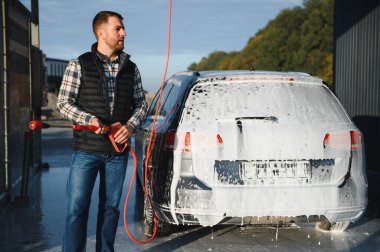 Araba yıkama ekipmanı. Bir adam oto yıkamada araba yıkarken yüksek basınçlı araç yıkama makinesi köpük püskürtür..