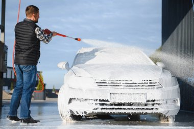 Araba yıkamada yıkanır, adam arabayı köpükle yıkar. Ayrıntılar.