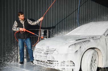 Bir adam arabayı yıkarken köpüğü yıkar. Bir araç araba yıkama sırasında sabunlu köpüğe bulanır, lastikleri, tekerlekleri, kaputu ve arabanın tüm dış kısmını kaplar. self-servis araba yıkama