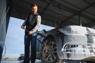 Bir adam arabayı yıkarken köpüğü yıkar. Bir araç araba yıkama sırasında sabunlu köpüğe bulanır, lastikleri, tekerlekleri, kaputu ve arabanın tüm dış kısmını kaplar. self-servis araba yıkama