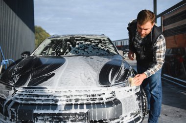 Süngerli bir işçi arabayı köpükle yıkar. Araba yıkama ve araba bakımı.