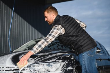 Bir adam oto yıkamada bir arabayı süngerle yıkar..