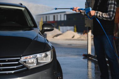 Adam yüksek basınçlı çamaşır makinesinden çıkan suyla araba yıkıyor..