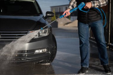 Bir adam arabasını tazyikli suyla yıkama makinesinde yıkıyor..