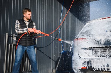 Bir adam arabayı yıkarken köpüğü yıkar. Bir araç araba yıkama sırasında sabunlu köpüğe bulanır, lastikleri, tekerlekleri, kaputu ve arabanın tüm dış kısmını kaplar. self-servis araba yıkama