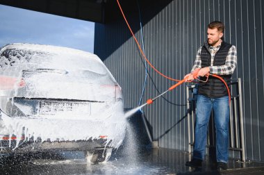Araba yıkama ekipmanı. Bir adam oto yıkamada araba yıkarken yüksek basınçlı araç yıkama makinesi köpük püskürtür..