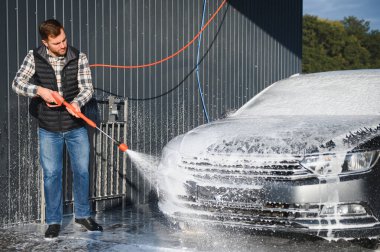 Araba yıkama ekipmanı. Bir adam oto yıkamada araba yıkarken yüksek basınçlı araç yıkama makinesi köpük püskürtür..