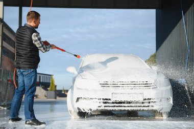 Araba yıkama ekipmanı. Bir adam oto yıkamada araba yıkarken yüksek basınçlı araç yıkama makinesi köpük püskürtür..
