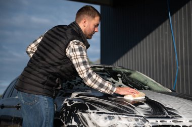 Süngerli bir işçi arabayı köpükle yıkar. Araba yıkama ve araba bakımı.