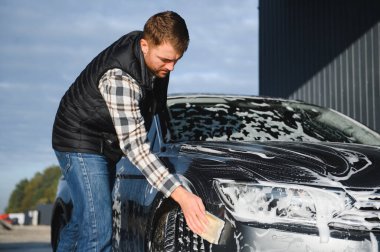 Bir adam oto yıkamada bir arabayı süngerle yıkar..