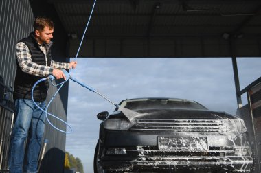 Adam yüksek basınçlı çamaşır makinesinden çıkan suyla araba yıkıyor..