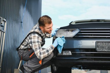 Araba temizliği, yıkama ve temizlik konsepti. Siyah lastik eldivenli, genç, sakallı, profesyonel araba yıkayıcı. Mikrofiber tutuyor ve lüks araba siliyormuş..