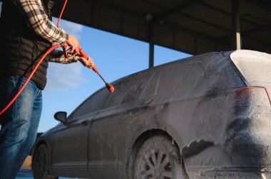 Bir adam arabayı yıkarken köpüğü yıkar. Bir araç araba yıkama sırasında sabunlu köpüğe bulanır, lastikleri, tekerlekleri, kaputu ve arabanın tüm dış kısmını kaplar. self-servis araba yıkama