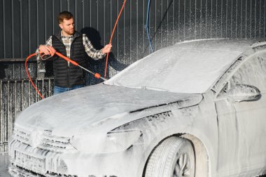 Araba yıkama ekipmanı. Bir adam oto yıkamada araba yıkarken yüksek basınçlı araç yıkama makinesi köpük püskürtür..